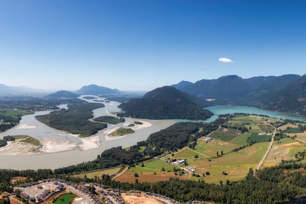Aerial view of the Fraser River winding past farmland and mountains in the Fraser Valley Regional District, BC